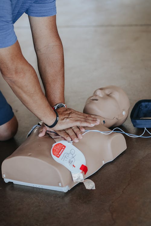 Hands performing CPR compressions on training mannequin with AED pads attached